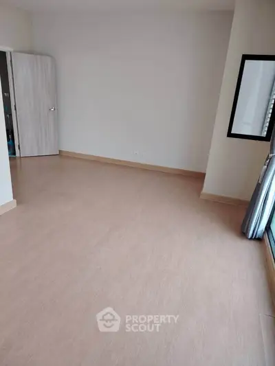 Spacious empty room with wooden flooring and large window, perfect for customization.