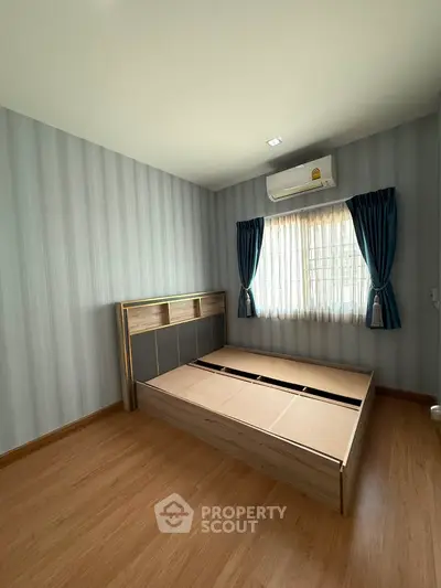 Spacious bedroom with wooden flooring and natural light, featuring a modern bed frame and air conditioning.
