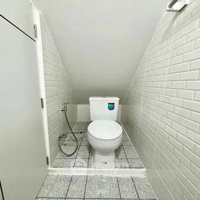Compact bathroom with modern white tiles and sloped ceiling design.