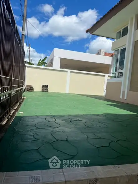Spacious outdoor area with green paved surface and modern building exterior, perfect for relaxation.