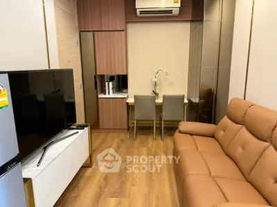 Modern living room with brown leather sofa and flat-screen TV, featuring elegant wood flooring.