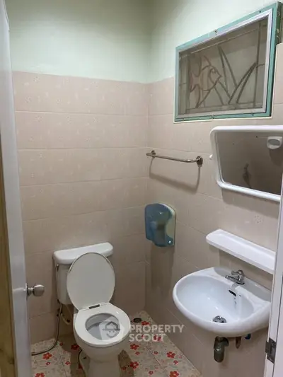 Compact bathroom with toilet, sink, and wall-mounted mirror in a tiled setting.