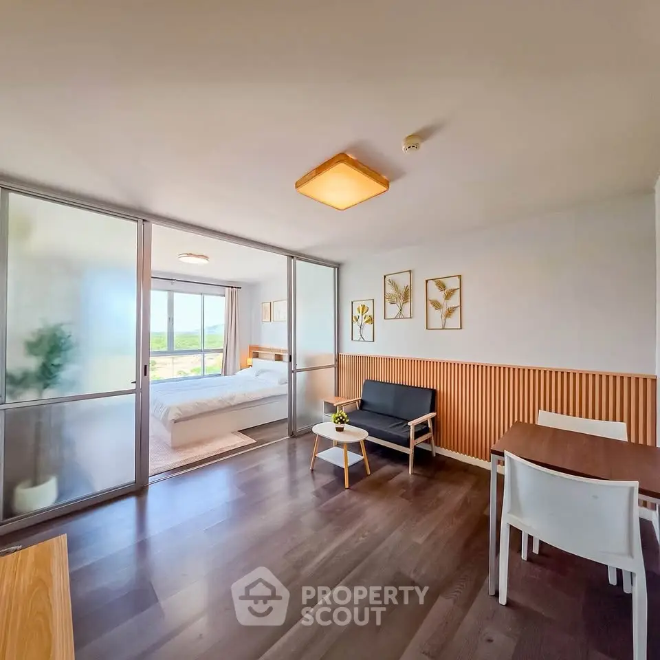 Modern open-plan living room with sliding doors leading to a bright bedroom, featuring stylish decor and wooden flooring.
