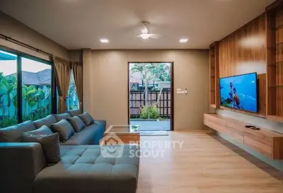 Spacious modern living room with large sofa and wall-mounted TV, overlooking a lush garden view.