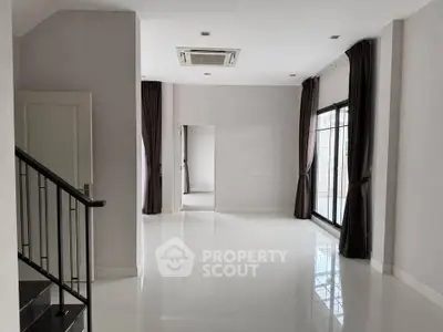 Spacious modern living room with large windows and sleek staircase, perfect for contemporary living.