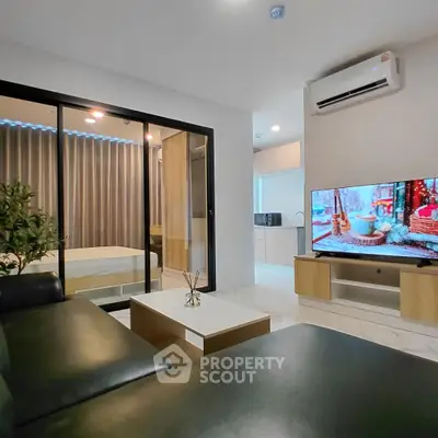 Modern living room with sleek black sofa, flat-screen TV, and sliding glass doors to bedroom.