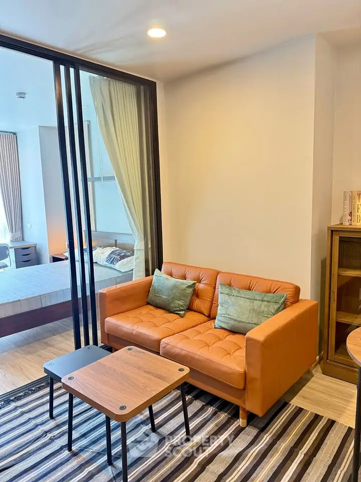 Modern living room with cozy orange sofa and stylish decor adjacent to a bedroom with glass partition.