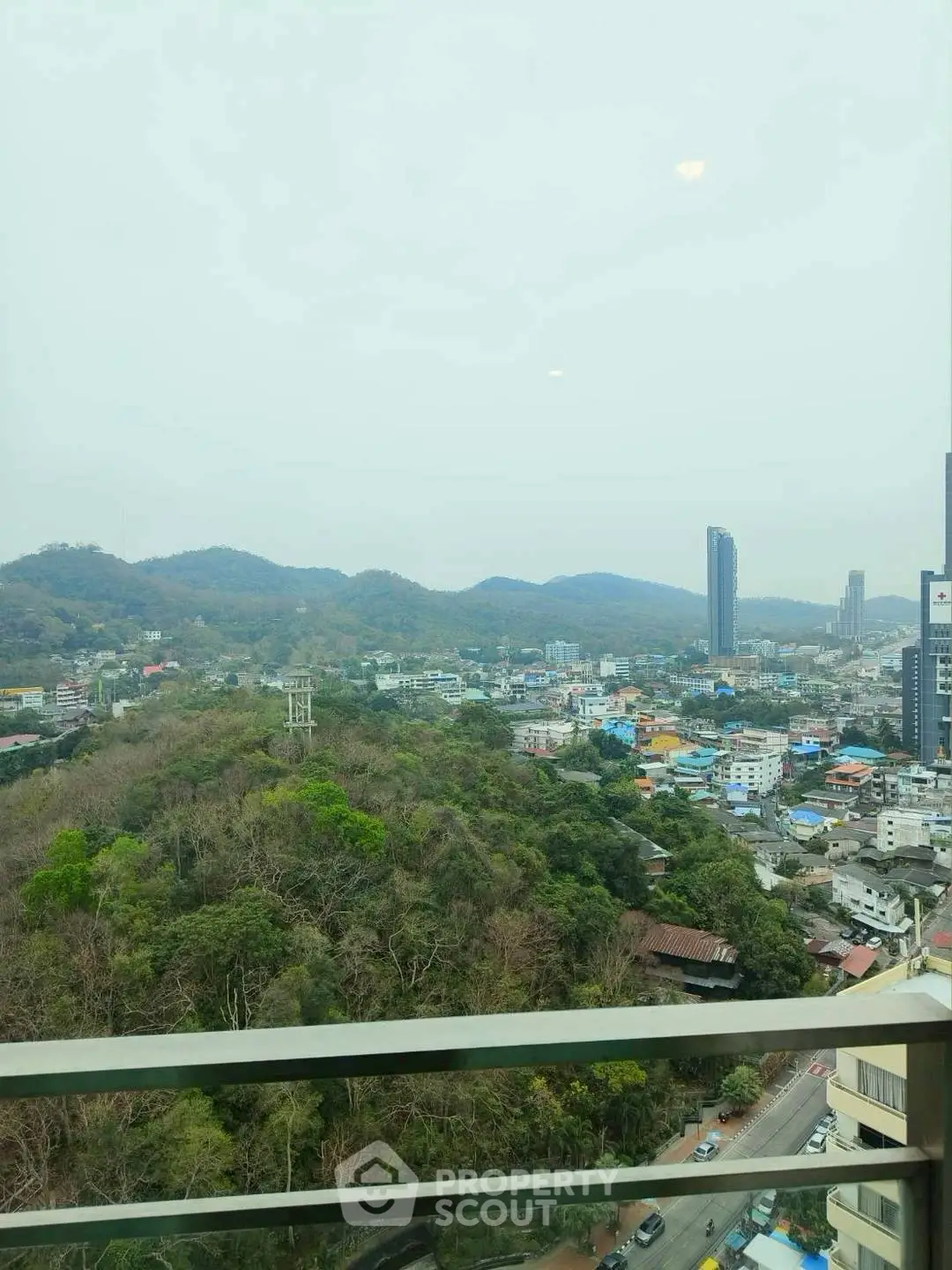 Stunning cityscape view from high-rise balcony overlooking lush hills and urban skyline.