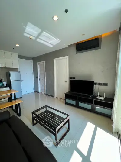 Modern living room with sleek furniture and natural light, featuring a TV and air conditioning unit.