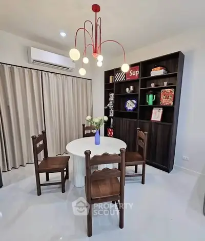 Charming dining area with modern chandelier and stylish bookshelf, perfect for cozy gatherings.