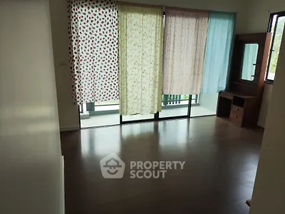 Spacious bedroom with large windows and wooden flooring, featuring a dresser and balcony access.