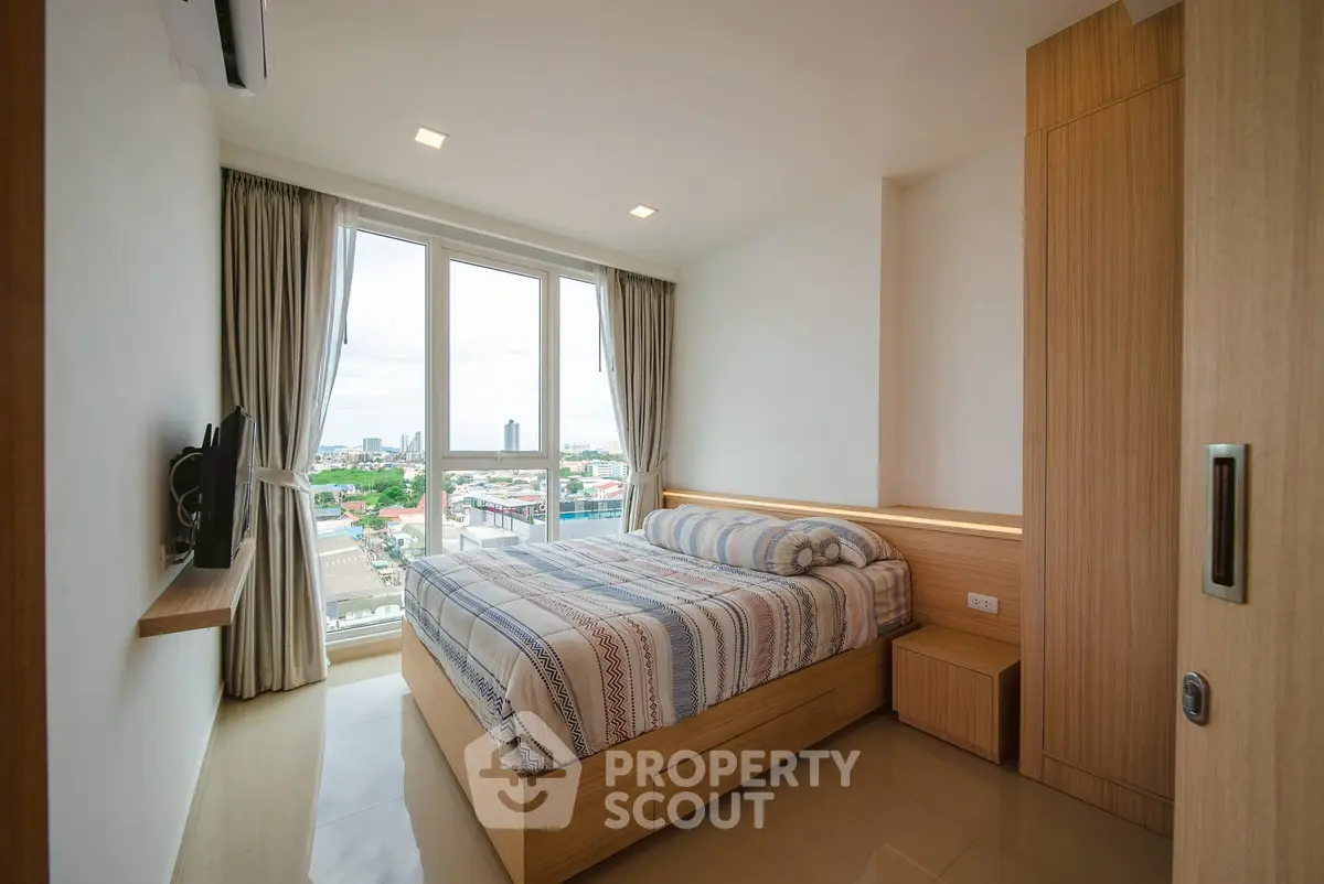 Modern bedroom with large window offering stunning city view, featuring cozy bed and sleek wooden furniture.