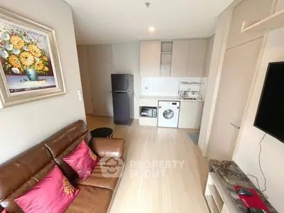 Modern living room with leather sofa, vibrant artwork, and compact kitchen featuring appliances.