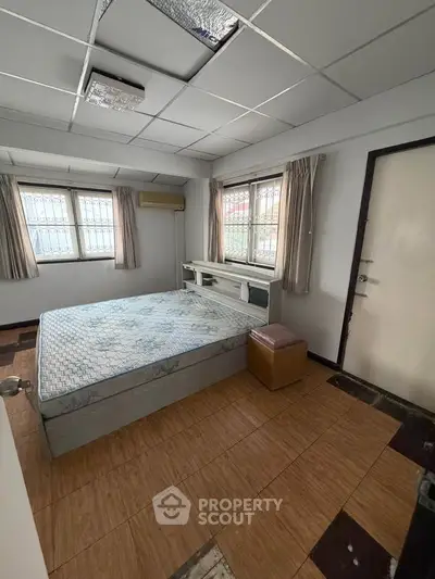 Cozy bedroom with natural light and minimalist decor, featuring a comfortable bed and tiled flooring.