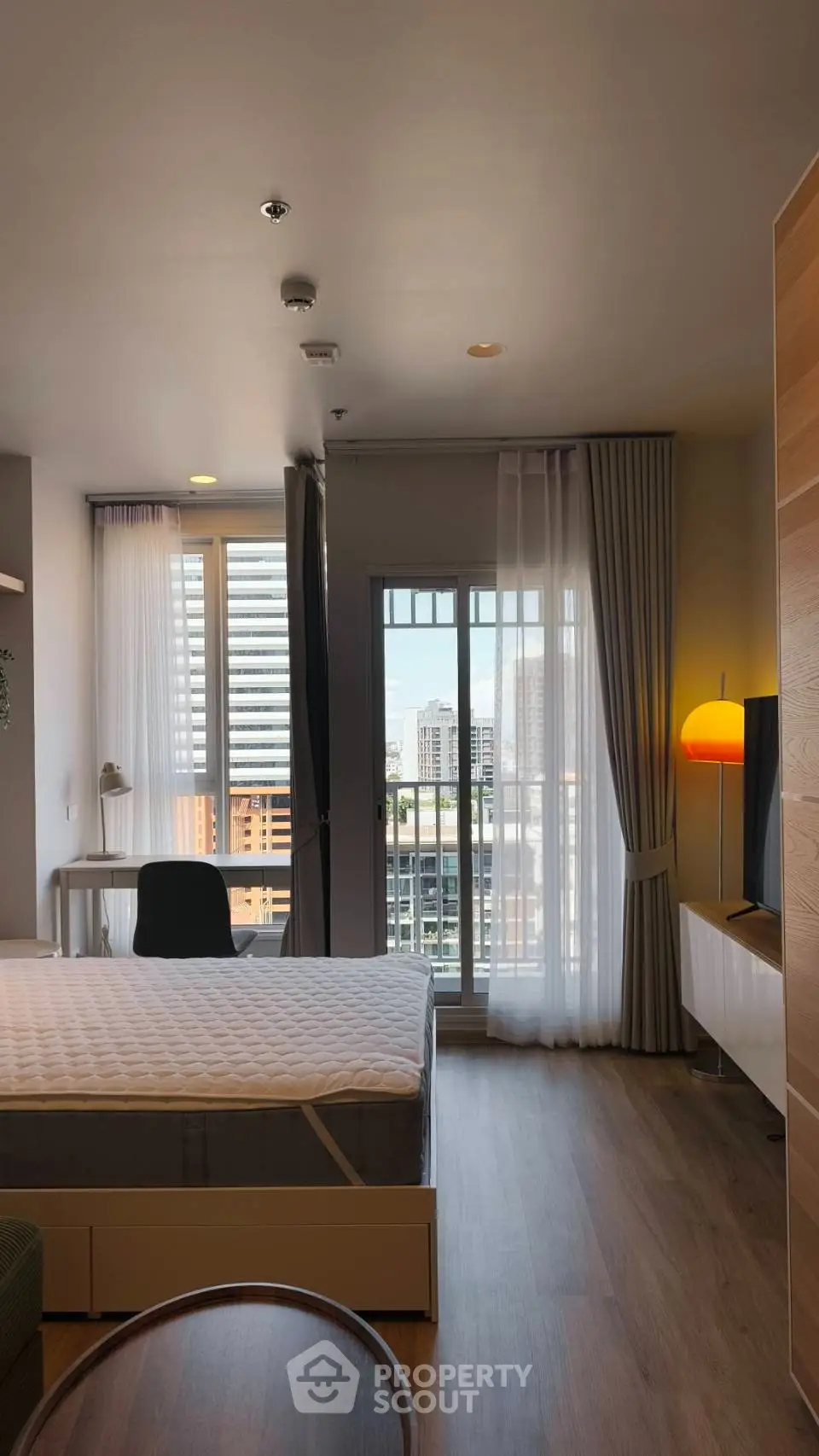 Modern bedroom with city view, featuring a cozy bed, stylish decor, and natural light through large windows.