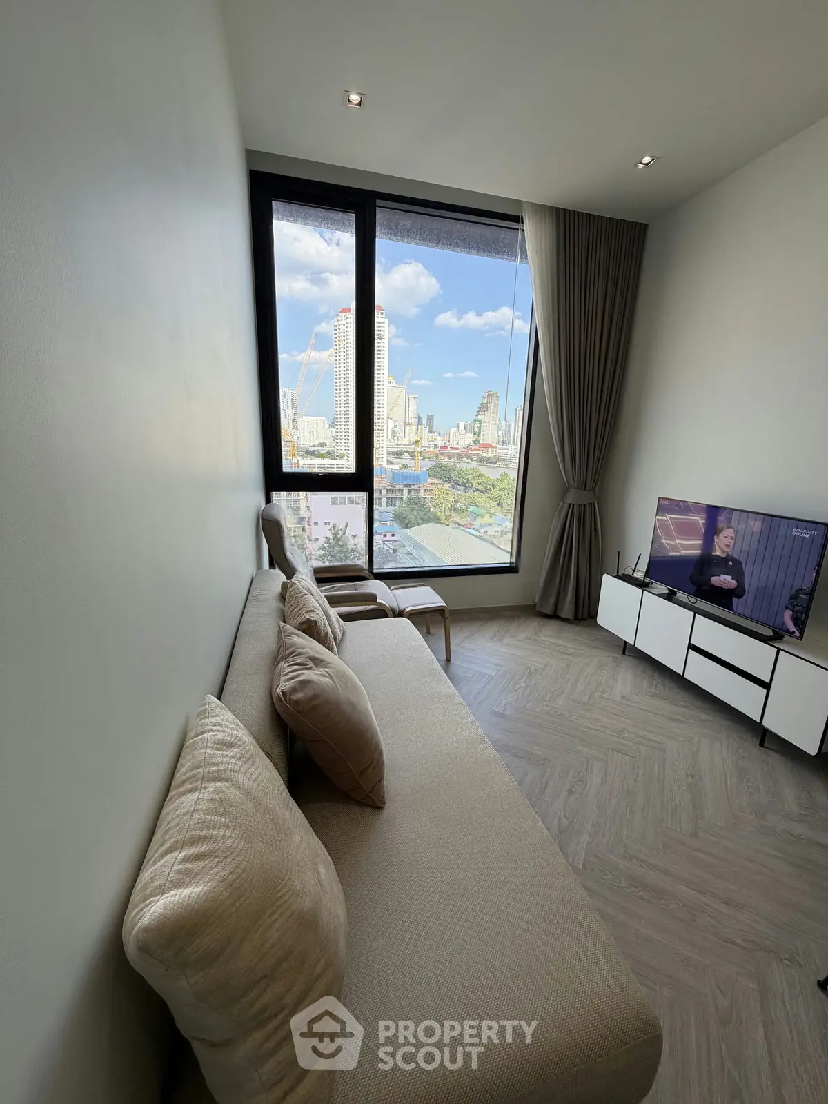 Modern living room with large window offering stunning city view, cozy sofa, and sleek TV setup.