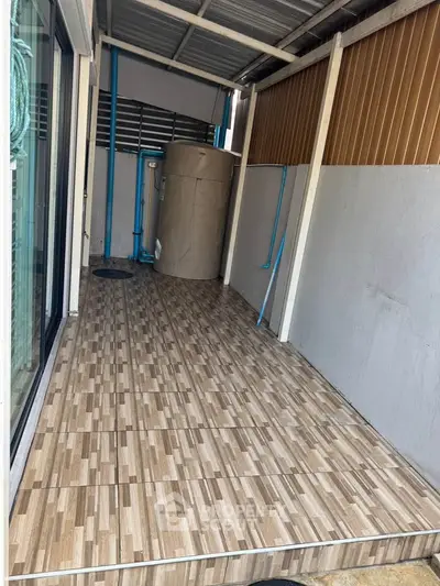 Covered outdoor area with tiled flooring and water tank, ideal for utility use.