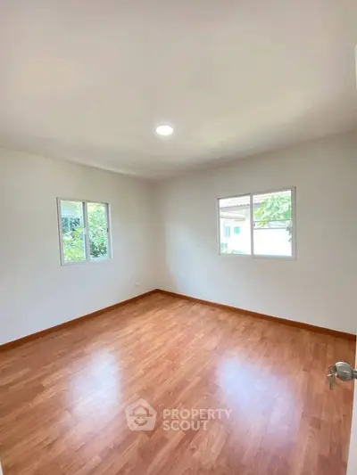 Spacious empty room with wooden flooring and natural light from two windows.
