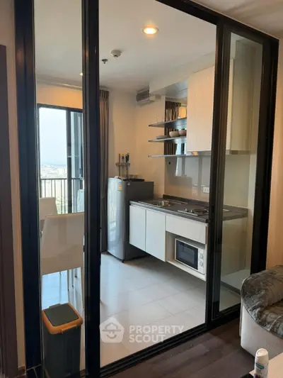 Modern kitchen with glass sliding doors and compact appliances in a stylish apartment.
