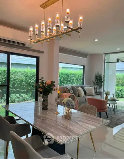 Elegant living room with modern chandelier and garden view, featuring stylish furniture and large windows.