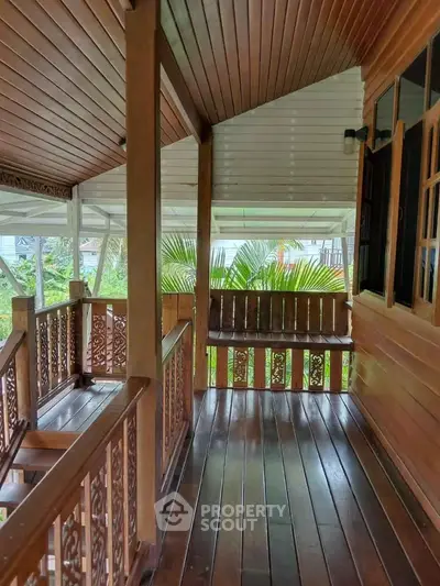 Charming wooden balcony with intricate railing and lush garden view, perfect for relaxation.