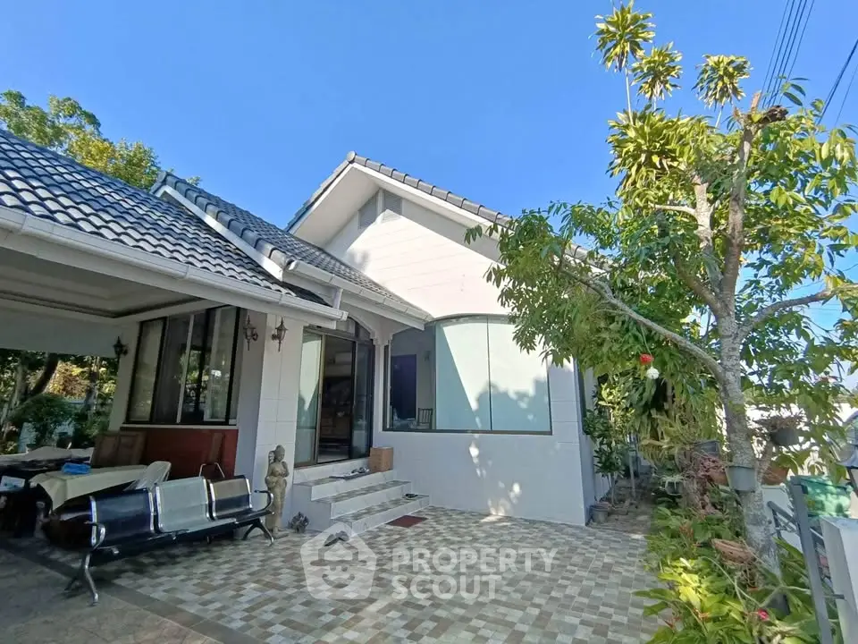 Charming single-story home with tiled patio and lush greenery under a clear blue sky.