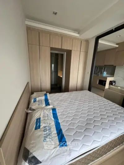 Modern bedroom with built-in wardrobe and kitchen view, showcasing compact urban living space.