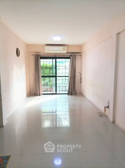 Spacious and well-lit living room with glossy tiled flooring, large windows draped with elegant curtains, and a serene view of greenery outside, perfect for a modern lifestyle.