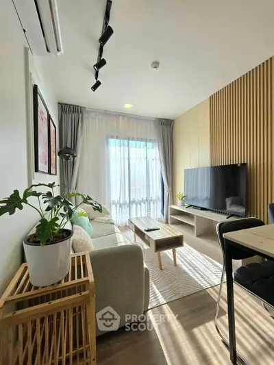 Modern living room with stylish decor, large TV, and natural light through sheer curtains.