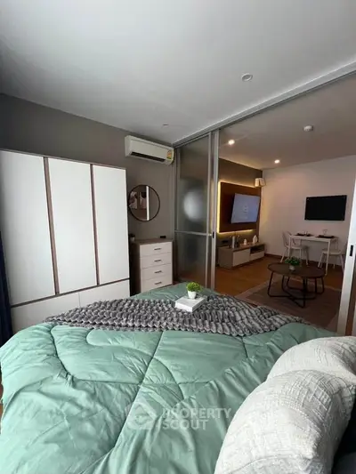 Modern bedroom with sliding doors leading to a stylish living area, featuring sleek furniture and ambient lighting.
