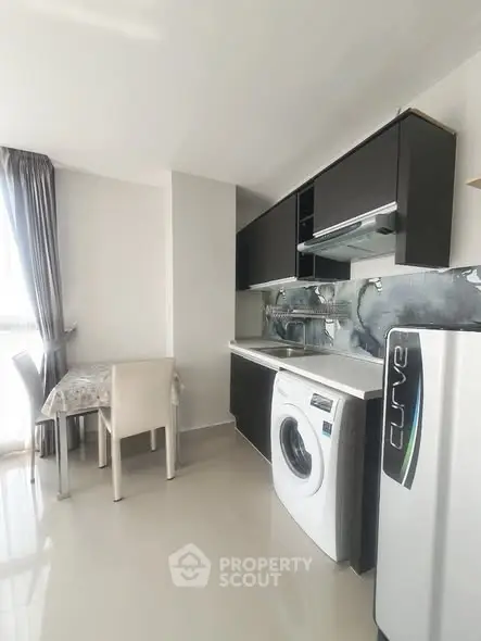 Modern kitchen with sleek cabinets, washing machine, and dining area in bright apartment.