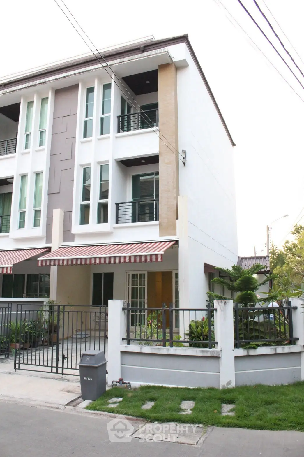 Modern three-story townhouse with stylish facade and small garden in a suburban neighborhood.