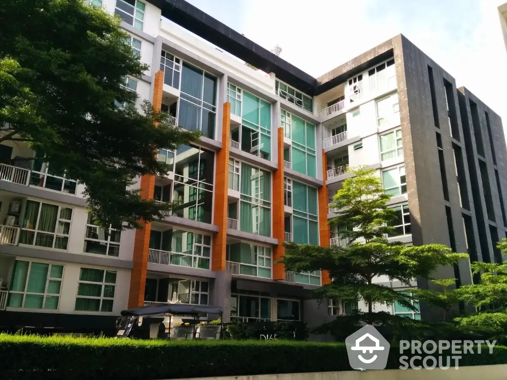 Modern apartment building with large windows and lush greenery in urban setting.