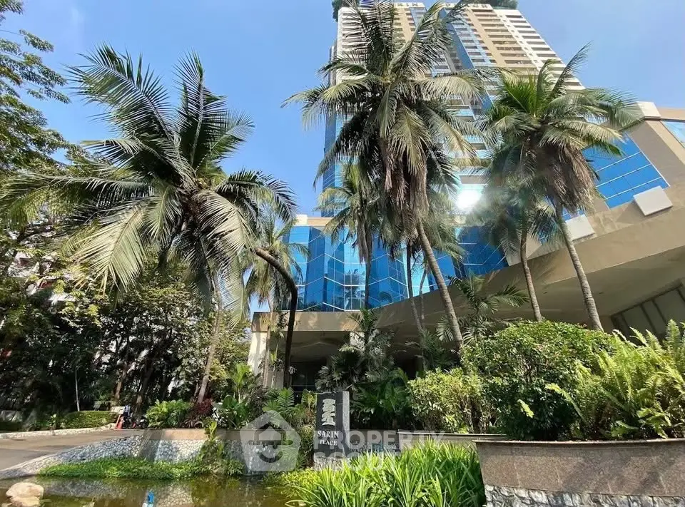 Luxurious high-rise building with lush tropical landscaping and modern glass facade.