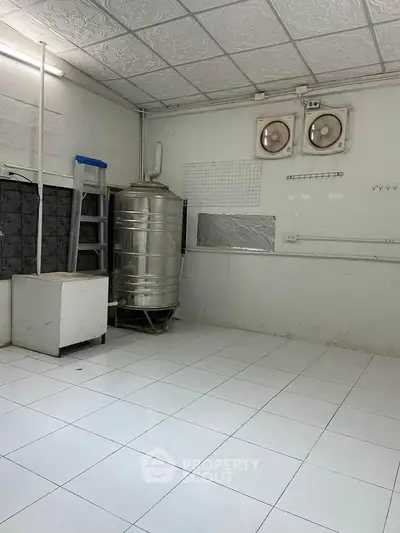 Spacious utility room with tiled floor and stainless steel water tank, ideal for storage or laundry setup.