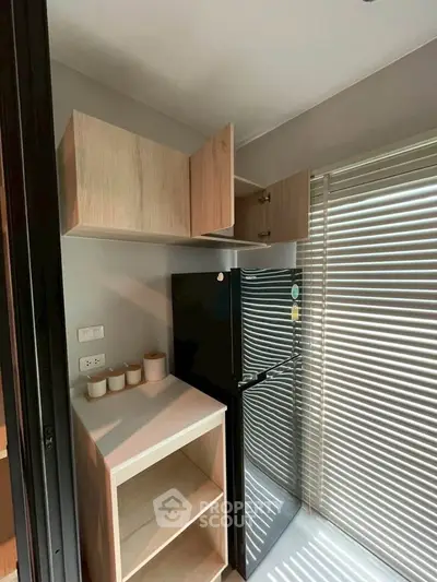 Modern kitchen corner with sleek black fridge and wooden cabinets, perfect for compact living spaces.