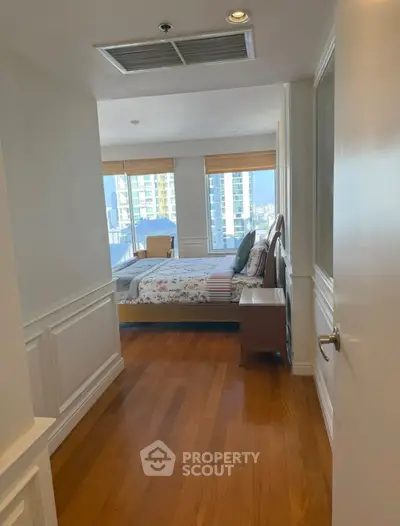 Spacious bedroom with wooden flooring and large windows offering city views.