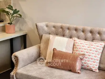 Elegant tufted sofa adorned with decorative pillows, complemented by a stylish plant and modern side table, perfect for a chic living space.
