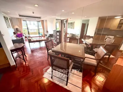 Spacious living room with elegant dining area and mirrored wall, featuring hardwood floors and natural light.