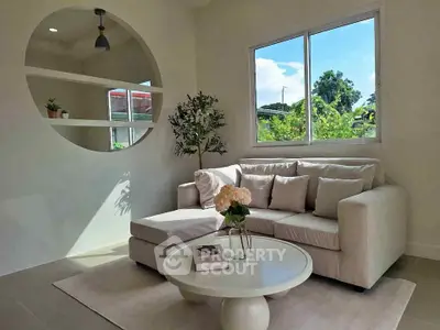 Chic living room with cozy sofa, round mirror, and lush garden view through window.