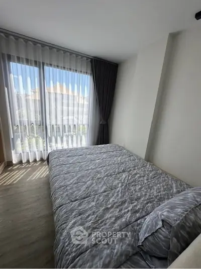 Bright bedroom with large windows and elegant curtains, featuring a cozy bed and modern decor.