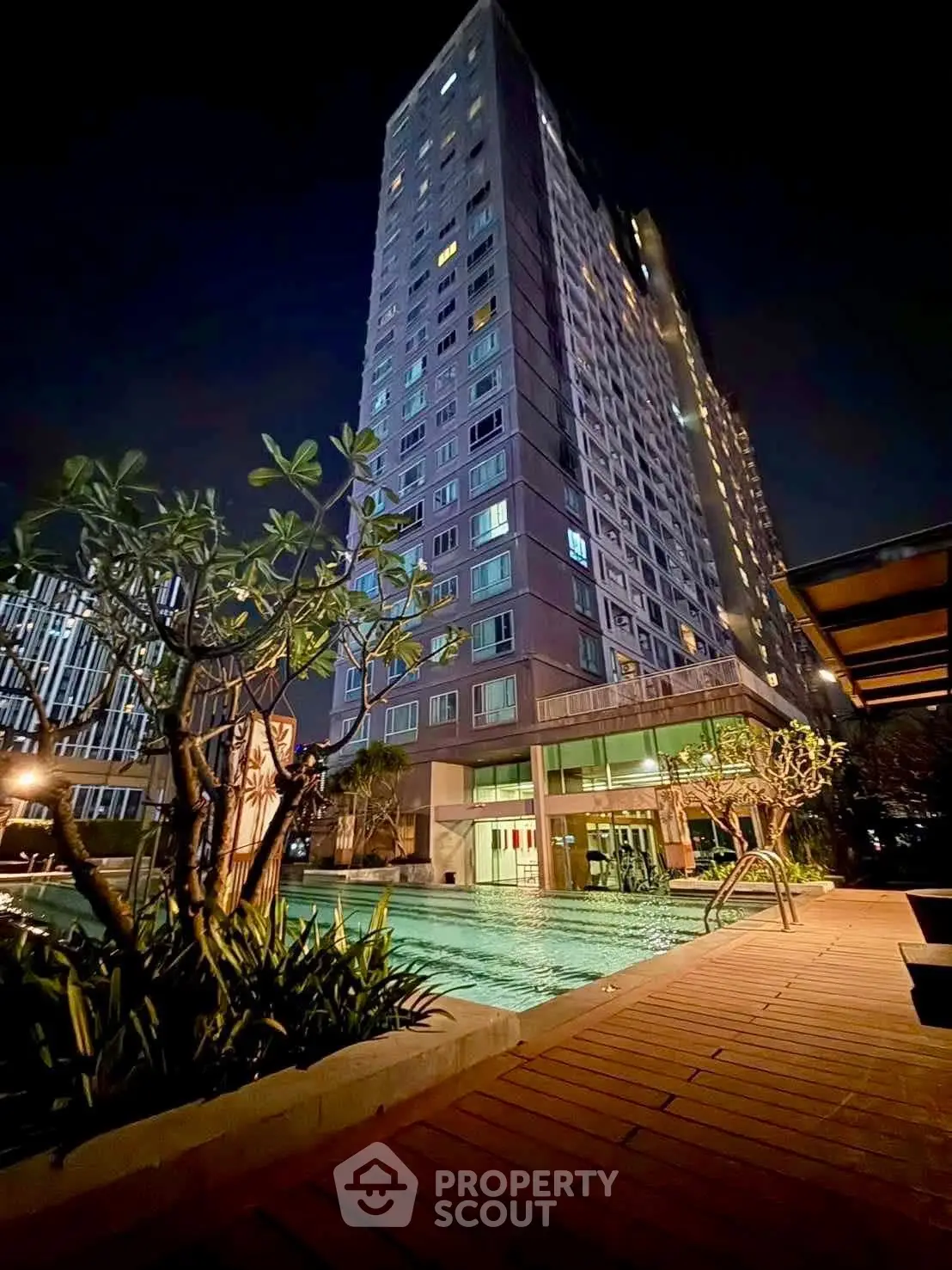 Stunning night view of modern high-rise building with illuminated poolside area, perfect for luxury living.