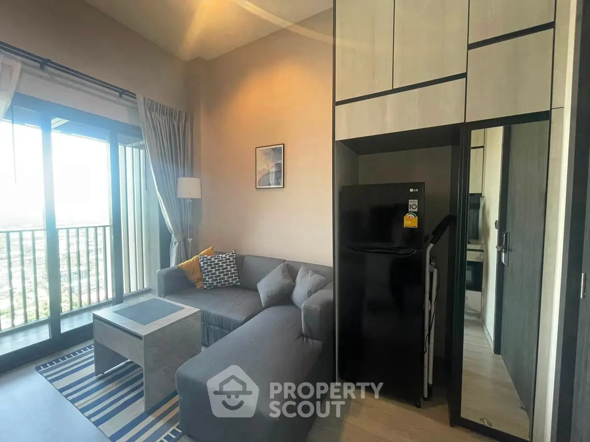 Modern living room with cozy sectional sofa and sleek black refrigerator, featuring a large window with city view.
