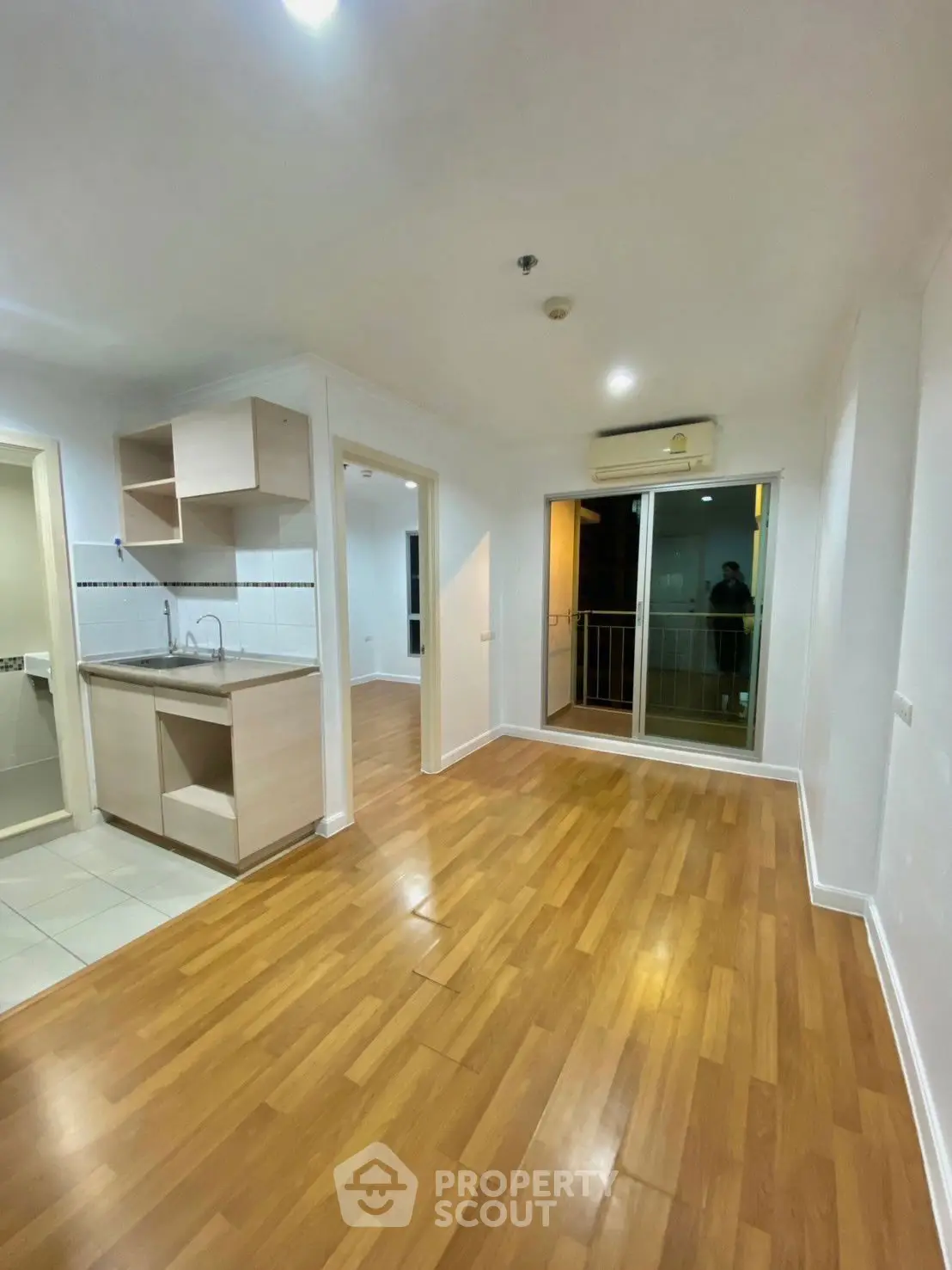 Modern apartment interior with open layout and balcony access, featuring sleek wooden flooring and compact kitchen.