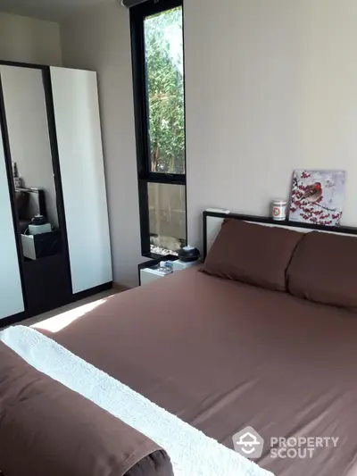 Cozy bedroom with a large comfortable bed, floor-to-ceiling window offering natural light, and a full-length mirror adding depth to the space.