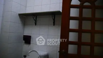 Cozy bathroom with tiled walls and wooden door, featuring a shelf above the toilet for added storage.
