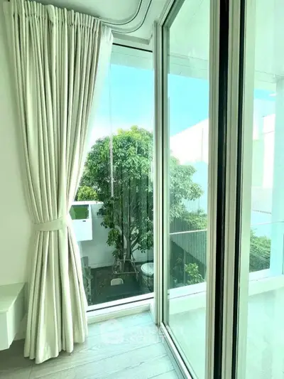 Bright modern balcony with floor-to-ceiling windows and lush garden view.