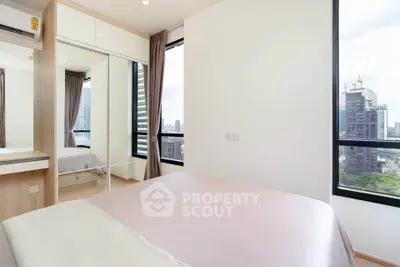 Modern bedroom with city view, featuring large windows and sleek mirrored wardrobe.