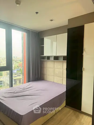 Modern bedroom with large window and city view, featuring sleek storage solutions and contemporary design.