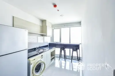 Modern kitchen with sleek appliances and natural light, featuring a washing machine and breakfast bar.